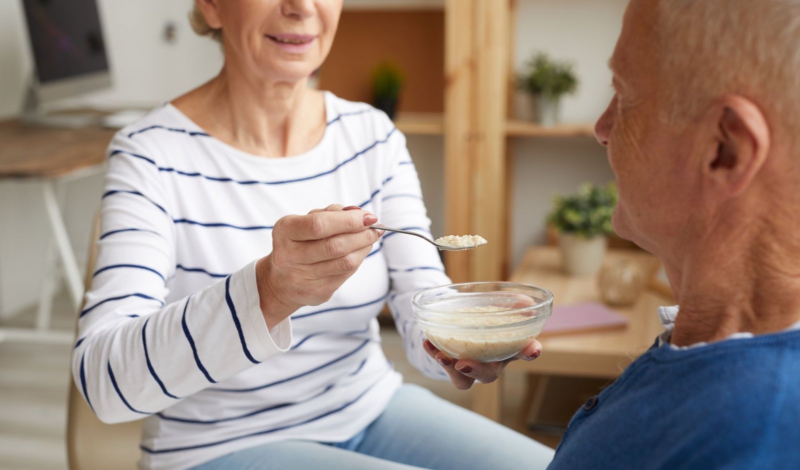 A senior woman feeds oatmeal to her spouse
