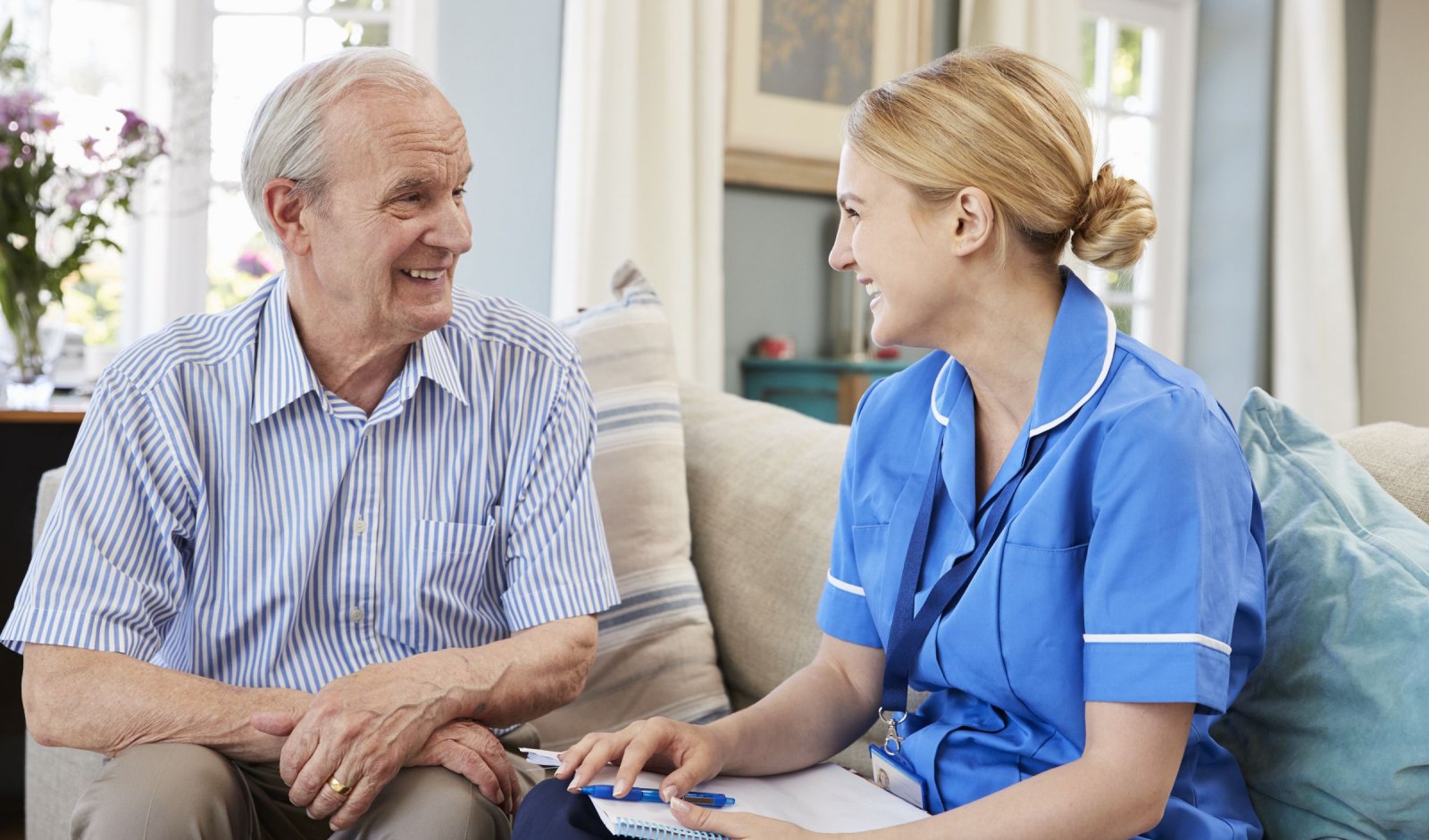 A senior man and his nurse smile as they have a discussion